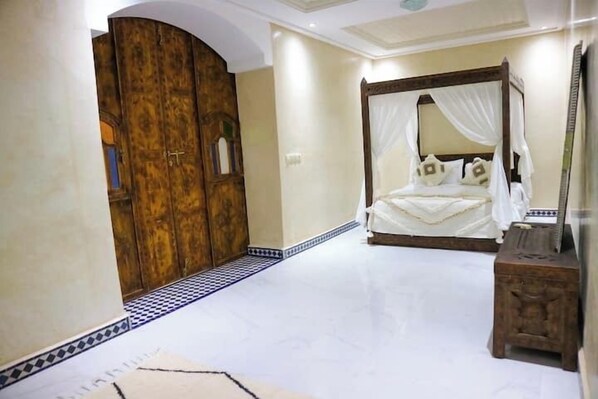 A bedroom with a four-poster bed, a wooden wardrobe, and a small wooden stool.
