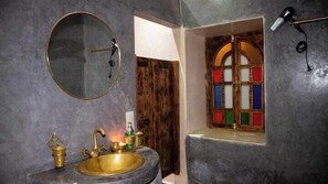 A bathroom with a round mirror, a sink with a brass faucet, and a wooden door with colorful stained glass.
