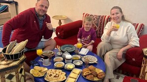 A family of three seated around a round table with a variety of food items and drinks. - RIAD RKIYA (Tiznit)