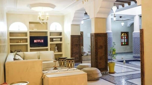 A modern living room with a sofa, ottoman, and a flat-screen TV displaying the Netflix logo. - RIAD RKIYA (Tiznit)