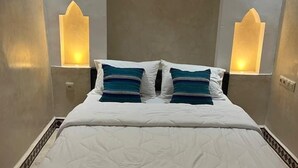 A bed with a white quilted cover and two pillows, flanked by two wall-mounted light fixtures with a geometric design. - RIAD RKIYA (Tiznit)