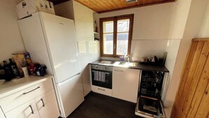 A compact kitchen with a refrigerator, oven, dishwasher, and a window providing natural light. - Swiss mountain chalet, wooden interior, cosy, with a beautiful view (Evolène)
