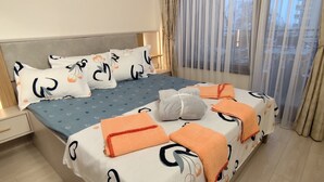 Un llit ben fet amb almoinades estampades, un edredó blau i tovalloles taronges.