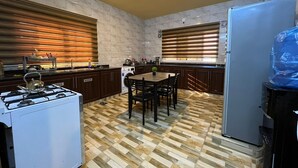 Una cocina con estufa a gas, armarios de madera, una mesa de comedor con sillas y un refrigerador.