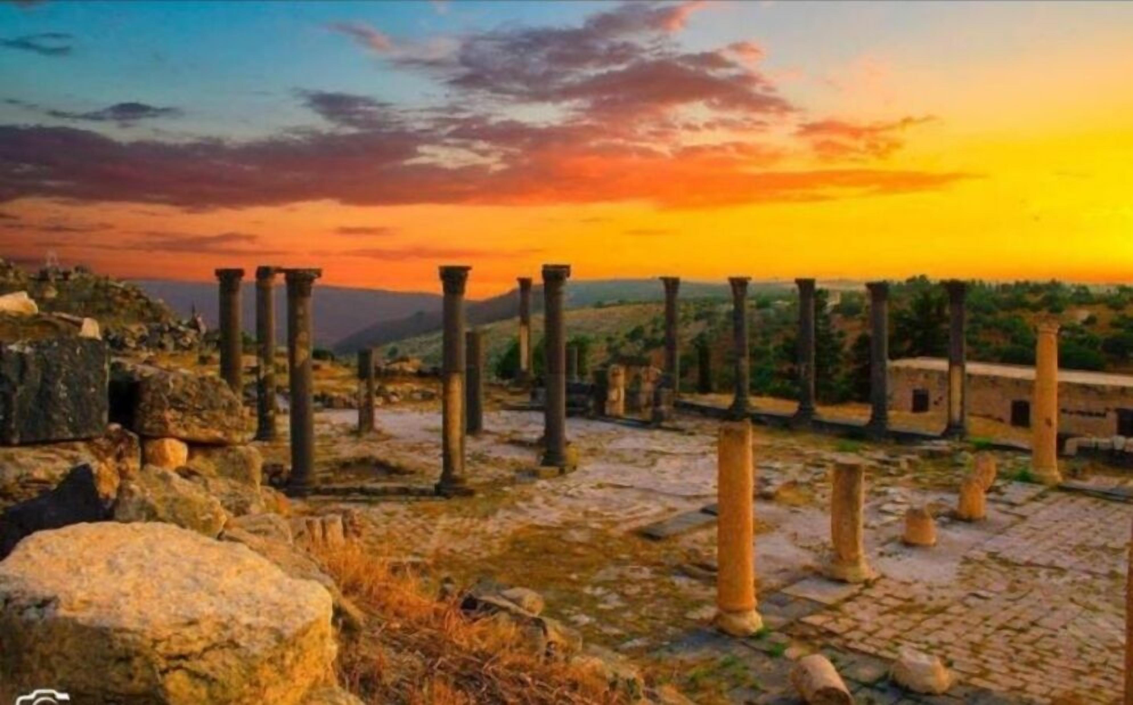 Ruinas antiguas con columnas y estructuras de piedra, al atardecer.