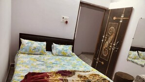 A bed with floral bedding, a red throw blanket, and a wooden headboard. - Hotel Gayatri Palace (Chandauli)