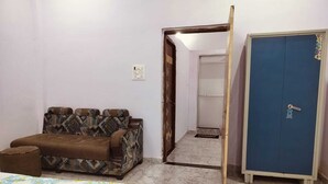 A room with a patterned sofa, a bed with a floral bedspread, a blue wardrobe, and a door leading to another room. - Hotel Gayatri Palace (Chandauli)