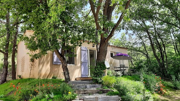 A rustic house with a wooden door, a small porch, and a garden with red flowers and greenery. - Country cottage, calm and relaxation in the sun. (Sainte-Croix-à-Lauze)