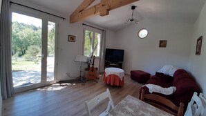 A living room with a wooden ceiling, a TV, a guitar, a table with a red tablecloth, and a couch. - Country cottage, calm and relaxation in the sun. (Sainte-Croix-à-Lauze)
