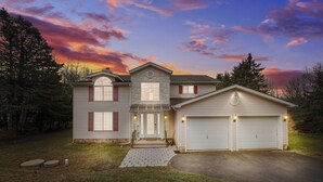 A two-story house with a front porch, a garage, and a driveway. - SPACIOUS 6-bedroom house with TWO MASTER BR AND BA, GAME ROOM, HOT TUB (Long Pond)
