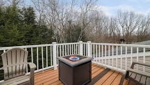 A deck with a built-in fire pit, white railings, and a view of trees. - SPACIOUS 6-bedroom house with TWO MASTER BR AND BA, GAME ROOM, HOT TUB (Long Pond)