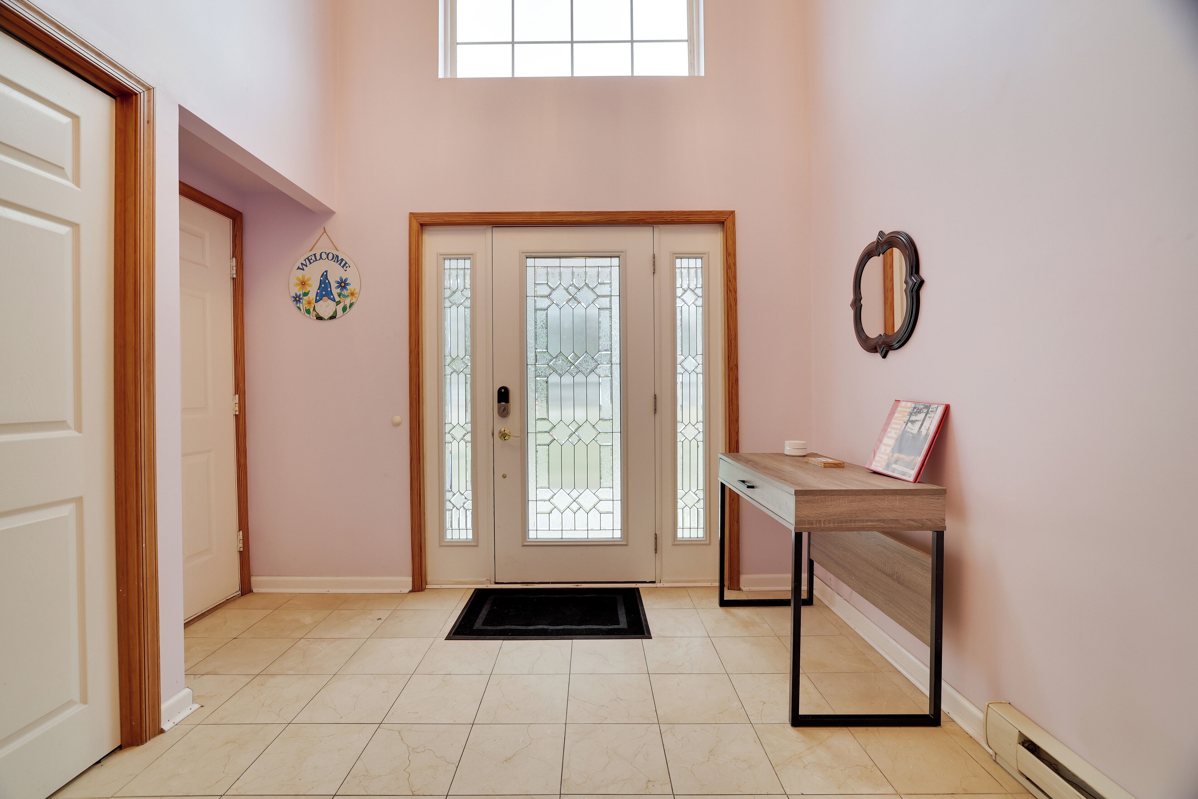 Un pasillo con una puerta de madera, un cartel de bienvenida, una puerta de cristal con un diseño decorativo y una mesa con un libro.