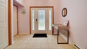 A hallway with a wooden door, a welcome sign, a glass door with a decorative pattern, and a table with a book. - SPACIOUS 6-bedroom house with TWO MASTER BR AND BA, GAME ROOM, HOT TUB (Long Pond)