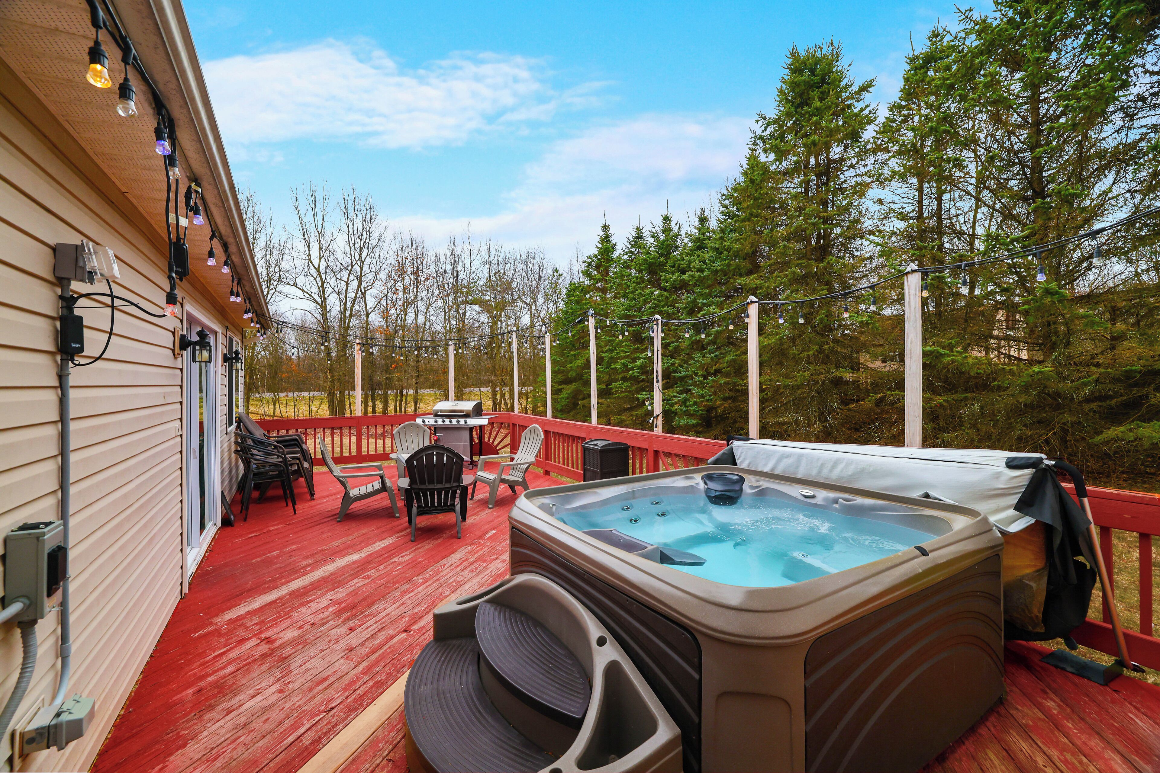 A hot tub on a wooden deck with outdoor seating and a barbecue grill.