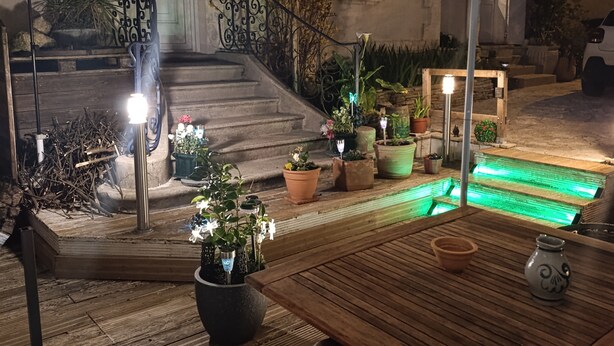 Un área de patio al aire libre con una mesa de madera, plantas en macetas, una escalera y un paraguas decorativo.