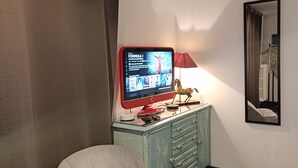Una habitación con televisión sobre un mueble, una silla, una lámpara y un espejo en la pared.