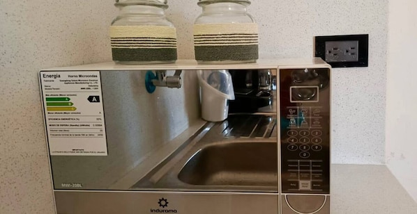 Et kompakt køkken i rustfrit stål med indbygget mikrobølgeovn og vask, der inkluderer et kontrolpanel og en stikkontakt på væggen.