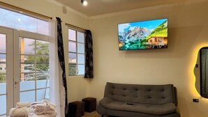 Une chambre d’hôtel avec un lit, un canapé gris, un téléviseur fixé au mur et une fenêtre avec des rideaux.