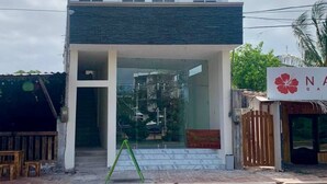 Un bâtiment à deux étages au design moderne, doté d’une grande entrée en verre et d’un espace extérieur aménagé en zone de repos, bien visible de l’extérieur.