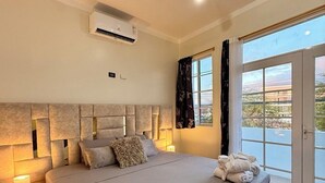 Ein modernes Schlafzimmer mit einem großen Bett, Nachttischlampen, einer Klimaanlage und Blick durch eine Schiebetür.