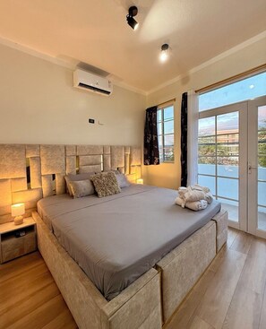 A modern bedroom with a large bed, bedside lamps, an air conditioning unit, and a view through a sliding glass door. - Golden Sand - Galapagos Home (Puerto Baquerizo Moreno, San Cristóbal)
