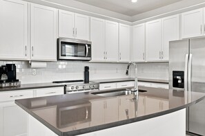 A modern kitchen with white cabinets, a stainless steel refrigerator, a built-in microwave, and a coffee maker.