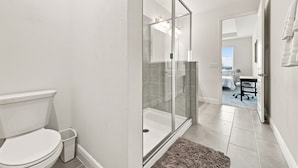 Een moderne badkamer met toilet, glazen douchecabine, en een zichtbare slaapkamer met bed en bureau.