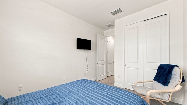 A bedroom with a bed, a chair, a television mounted on the wall, and a door leading to another room.