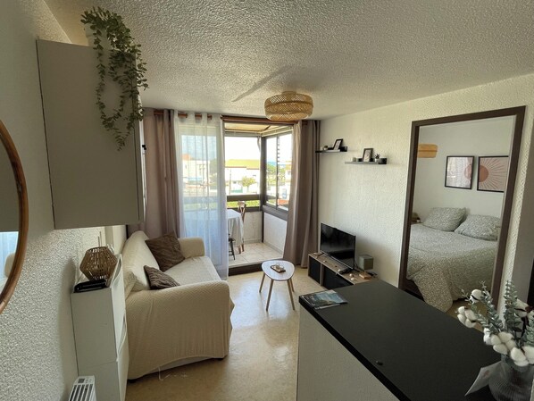 A modern living room with a sofa, a small table, a TV, and a balcony with curtains.