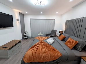 A modern hotel room with a large bed, a flat-screen TV, a small table, and a chair. - Spacious and Comfortable Modern Rooms (Clayton)