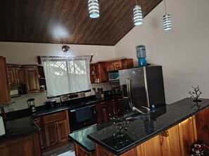 A kitchen with wooden cabinets, a stainless steel refrigerator, a water dispenser, and pendant lights.