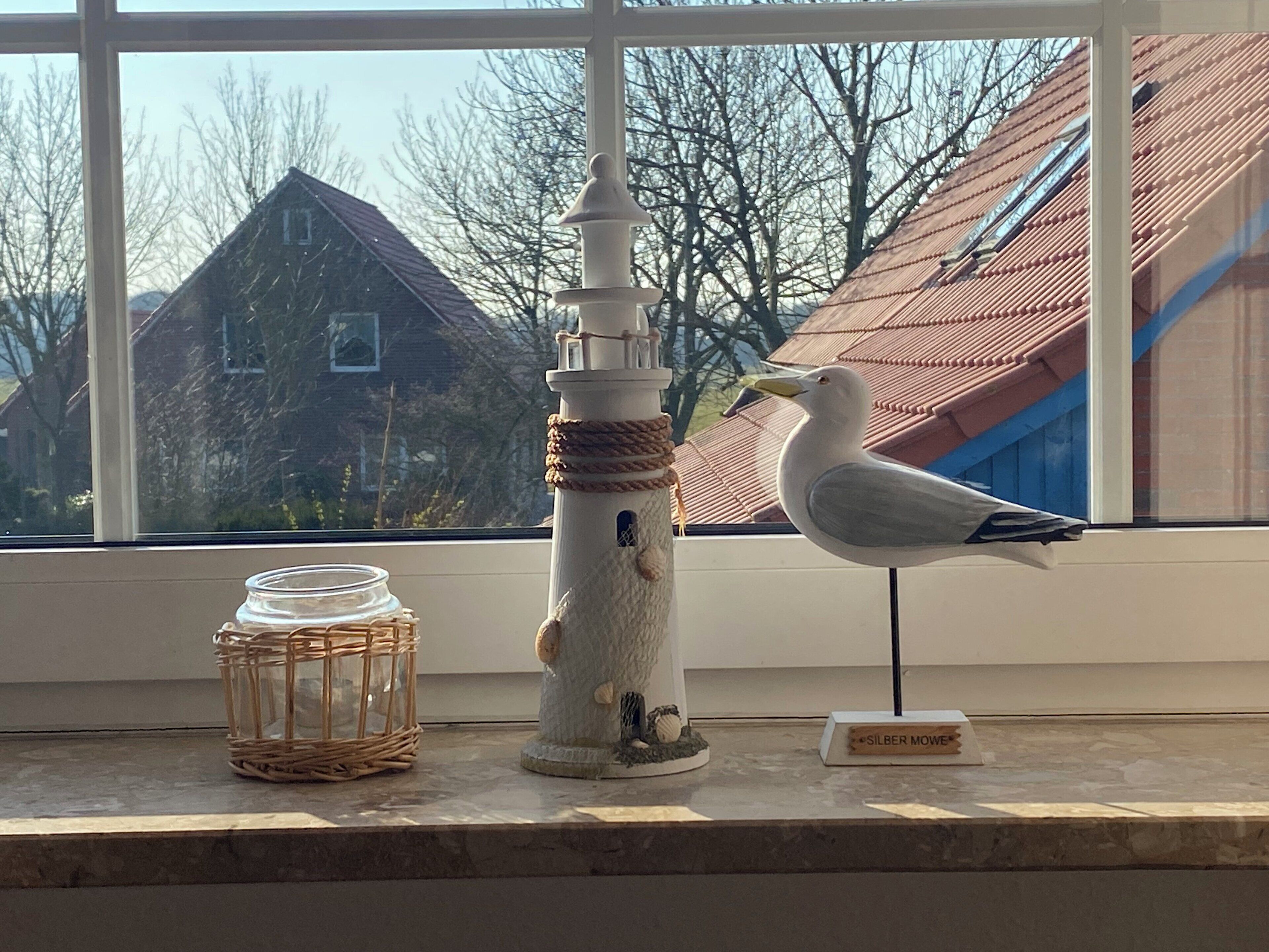 A window view of a house with a lighthouse ornament and a seagull figurine on a windowsill.