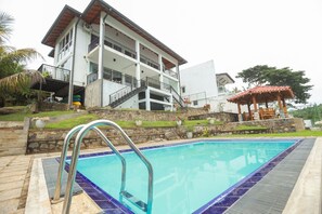Une piscine avec un escalier en métal, un immeuble à plusieurs étages doté de balcons et un espace de repos couvert avec un toit rouge.