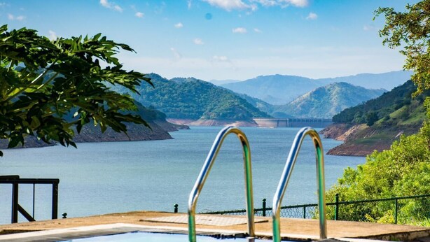 A swimming pool with metal railings, surrounded by lush greenery and a view of a large body of water with mountains in the background. - Villa Victoria Edge  (Digana)