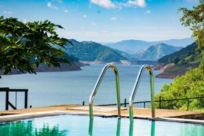 A swimming pool with metal railings, surrounded by lush greenery and a view of a large body of water with mountains in the background. - Villa Victoria Edge  (Digana)