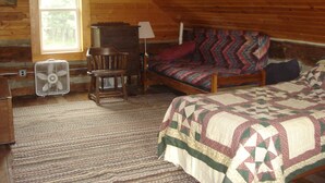 Un dormitorio acogedor en el ático con techo de madera, una cama con colcha colorida, una silla, un escritorio y una ventana.