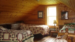 Un dormitorio acogedor tipo cabaña con dos camas, paredes de madera, una ventana y una lámpara.