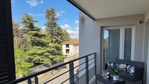 A balcony with a view of trees and a building, a small table with a plant, and a sofa. - Apartment with parking and balcony 200 m from the center (Avignon)