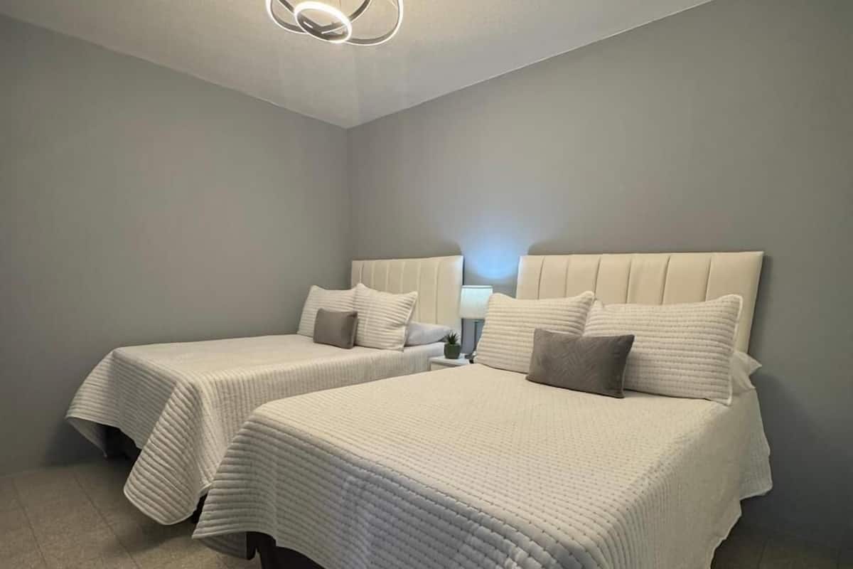 Une chambre d’hôtel moderne avec deux lits, un luminaire au plafond et une table de chevet avec une lampe.