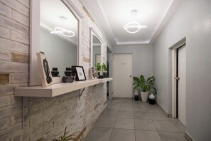 A hallway with a white brick wall, a white door, and a shelf with framed items and plants. - Ayari By Mondasch (Guatemala City)