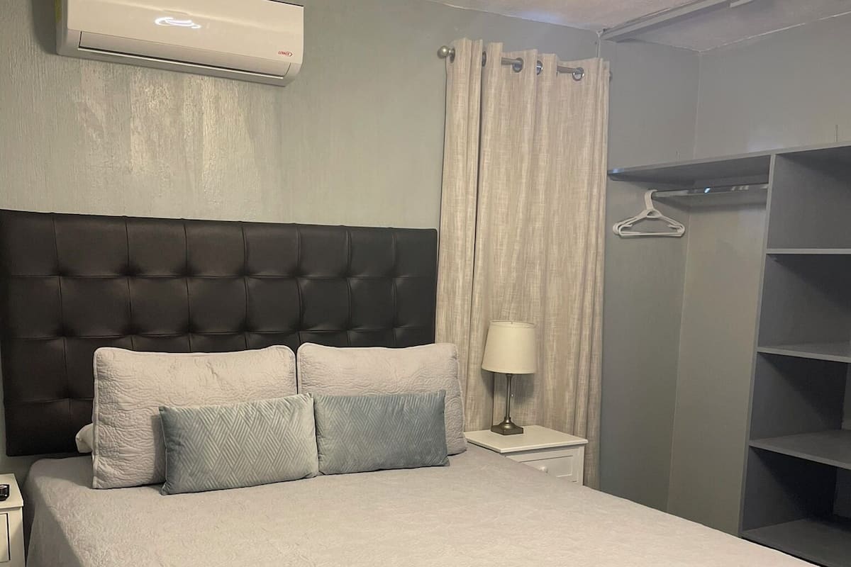Un lit bien fait, avec une tête de lit, une table de chevet avec une lampe et une armoire avec des étagères.