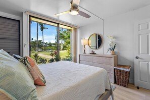 A bedroom with a bed, a dresser, a mirror, a ceiling fan, and a view of the outdoors.