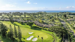 A golf course with a clubhouse, a large building in the background, and a view of the ocean.