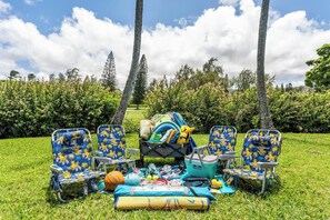 An outdoor setting with four beach chairs, a cooler, and various sports equipment on a grassy area.