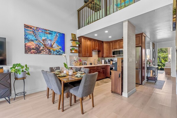 A modern kitchen with wooden cabinets, a dining area with a table and chairs, and a large painting on the wall.