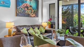 A modern living room with a leather sofa, green cushions, a coffee table, and a dining area with chairs and a wine glass.