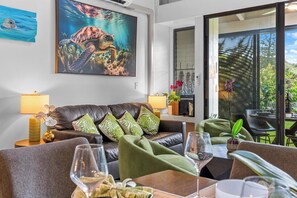 A modern living room with a leather sofa, green cushions, a coffee table, and a dining area with chairs and a wine glass. - Turtle Bay Hale: Fully Renovated 2025, Beach-Pool-Golf Course Frontage-A/C (Kahuku)