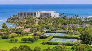 Un hotel con un edificio grande, cancha de tenis y vista al océano.