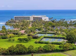 A hotel with a large building, a tennis court, and a view of the ocean.
