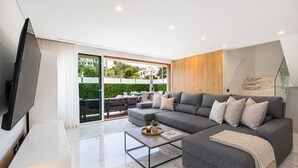 Una sala de estar moderna con un sofá grande de color gris, un televisor de pantalla plana y una mesa de centro de vidrio.